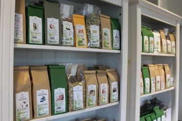 Tee-Variationen in braunen und grünen Verpackungen geordnet in weißen Regalen eines Tee-Shops.