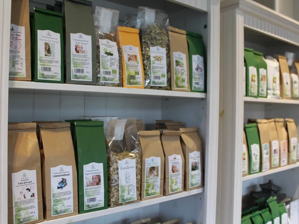 Tee-Shop Hiller Tee-Variationen in braunen und grünen Verpackungen geordnet in weißen Regalen eines Tee-Shops.