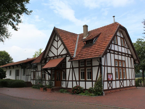 Fachwerkarchitektur des Hochzeitsbahnhofs Lavelsloh mit rotem Dach unter blauem Himmel.