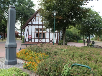 Hochzeitbahnhof Lavelsloh Historisches Fachwerkgebäude mit umliegendem Garten, Pflanzen und Parkbänken unter schattenspendenden Bäumen.