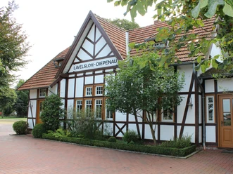 Hochzeitsbahnhof Lavelsloh Fachwerkgebäude mit gepflegtem Garten und Schildern, zeigt Hochzeitsbahnhof Lavelsloh in Niedersachsen.