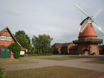 Landesbergen Hochzeitsmühle Historische Windmühle in Landesbergen mit rotem Backsteinsockel und weißen Flügeln, flankiert von Bäumen.