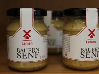 Drei Gläser Bauersenf von der Senffabrik Eystrup stehen auf einem Holzregal dicht nebeneinander.Three jars of Bauers mustard from the Eystrup mustard factory stand close together on a wooden shelf.Tre krukker med Bauers sennep fra Eystrups sennepsfabrik står tæt på hinanden på en træhylde.Drie potten Bauers mosterd van de Eystrup mosterdfabriek staan dicht bij elkaar op een houten plank.