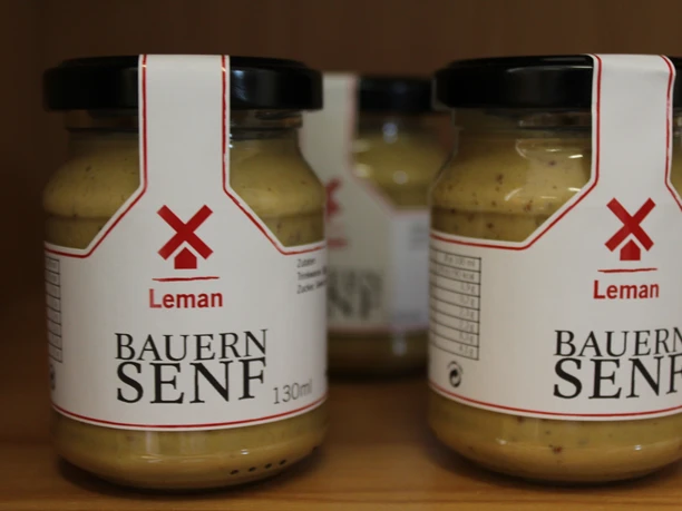 Three jars of Bauers mustard from the Eystrup mustard factory stand close together on a wooden shelf.