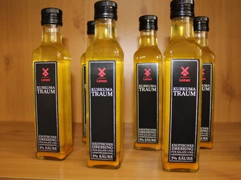 Essigflaschen Senffabrik Eystrup Sechs rechteckige Flaschen Kurkuma-Essig mit schwarzen Etiketten stehen eng beieinander auf Holzregal.Six rectangular bottles of turmeric vinegar with black labels stand close together on a wooden shelf.Seks rektangulære flasker med gurkemejeeddike med sorte etiketter står tæt sammen på en træhylde.Zes rechthoekige flessen kurkuma-azijn met zwarte etiketten staan dicht bij elkaar op een houten plank.