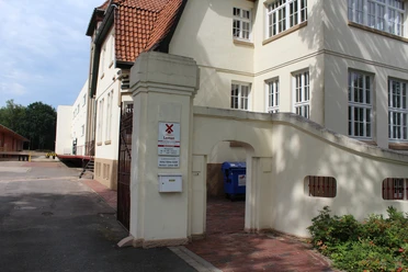 Entrance with brick archway to the historic Eystrup mustard factory, surrounded by white buildings.
