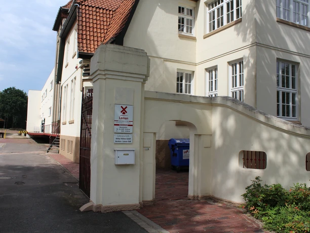Entrance with brick archway to the historic Eystrup mustard factory, surrounded by white buildings.
