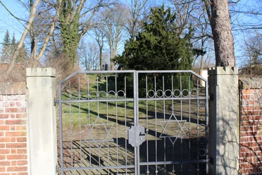 Jüdischer Friedhof Nienburg Metalltor mit Davidstern-Motiven öffnet den Zugang zu einem von Bäumen umgebenen Friedhof.