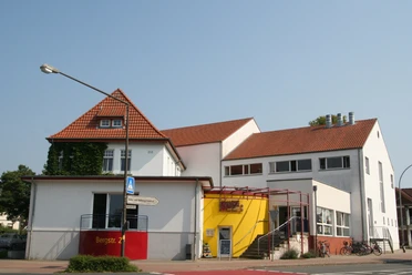 Kulturhaus mit rotem Ziegeldach und gelber Eingangsfassade; moderne Architektur und zweckmäßig.