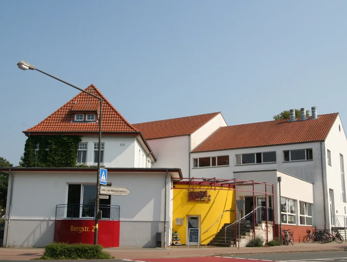 Kulturhaus mit rotem Ziegeldach und gelber Eingangsfassade; moderne Architektur und zweckmäßig.