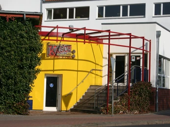 KASCH Kulturhaus mit gelber Fassade, barrierefreier Zugang, rote Stahlträger, begrüntes Umfeld.