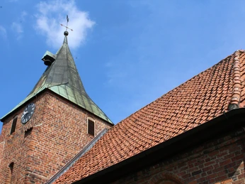 Backsteinkirche mit spitzem Kupferturm und Uhr vor blauem Himmel; markantes Beispiel norddeutscher Baukunst.