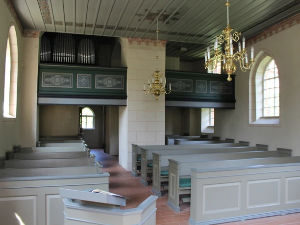 Orgel in einer schlichten Kirche mit Holzbänken und hölzernen Emporen, gekrönt von prächtigen Kronleuchtern.