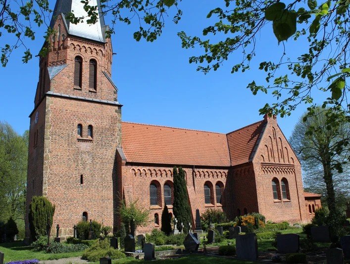 Historische Backsteinkirche mit markantem Turm und grüner Umgebung an einem klaren blauen Himmel.