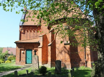 Kirche Magelsen Backsteinkirche mit grünem Tor, umgeben von Bäumen und Gräbern, im ländlichen Magelsen.