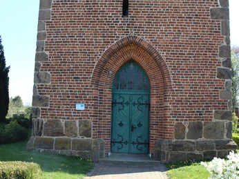 Kirche Magelsen Backsteinkirche in Magelsen mit grünem Holzportal und gotischem Spitzbogen, umgeben von gepflegtem Grün.