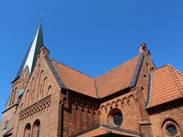 Backsteinkirche im gotischen Stil mit markantem Kirchturm und einem strahlend blauen Himmel im Hintergrund.