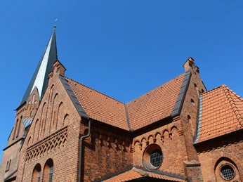 Kirche Magelsen Backsteinkirche im gotischen Stil mit markantem Kirchturm und einem strahlend blauen Himmel im Hintergrund.
