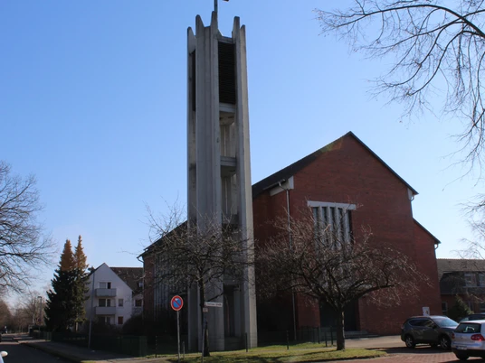Backsteinkirche St. Bernward mit markantem Eingangsturm, umgeben von Bäumen und wolkenlosem Himmel.