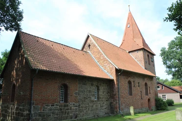 Kirche St. Cosmae et Damiani Hassel Backsteinkirche mit markantem Turm und rötlichen Dachziegeln, umgeben von grünen Bäumen und Mauerwerk.