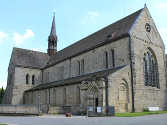 Romanesque façade of Loccum Abbey with high windows and a pointed tower under a clear sky.