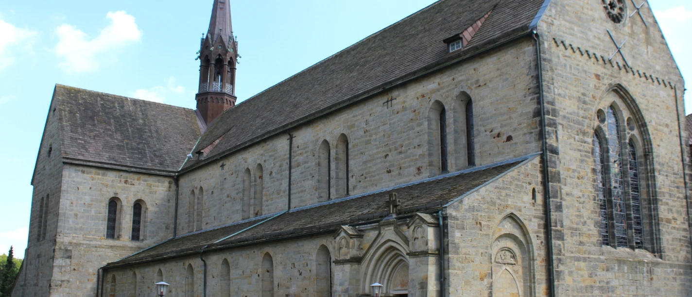 Kloster Loccum Loccum-klostrets romanske facade med høje vinduer og et spidst tårn under en klar himmel.
