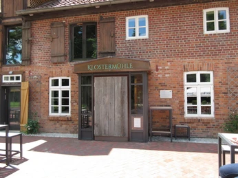 Brick building of the monastery mill with central wooden gate, flanked by windows; sign above the entrance.