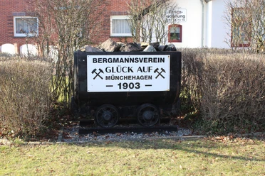 Kohlelore in Münchehagen Eine alte Kohlelore beladen mit Kohlen vor einer Hecke und Schildern des Bergmannsvereins Münchehagen.