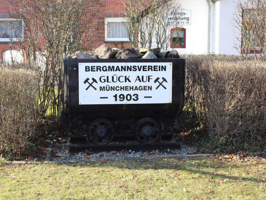 Kohlelore in Münchehagen Eine alte Kohlelore beladen mit Kohlen vor einer Hecke und Schildern des Bergmannsvereins Münchehagen.