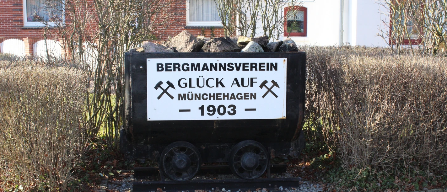 Kohlelore in Münchehagen Eine alte Kohlelore beladen mit Kohlen vor einer Hecke und Schildern des Bergmannsvereins Münchehagen.