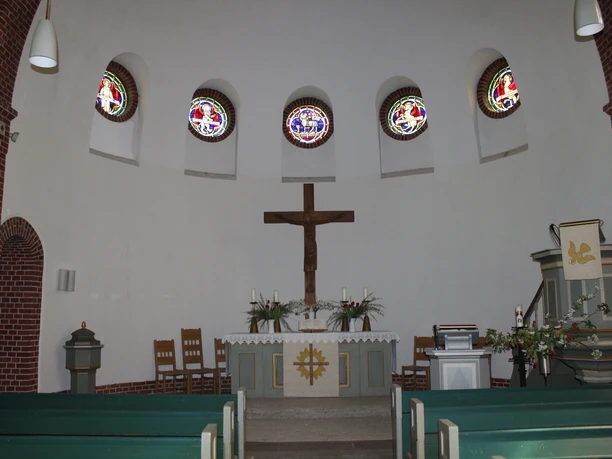 Innenraum der Kapelle Schweringen mit Altar, Kreuz, farbigen Kirchenfenstern und Holzbänken.