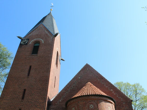 Backstein-Kapelle in Schweringen mit steilem Turm, blauem Himmel und umliegenden grünen Bäumen.