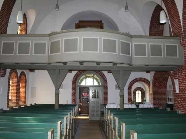 Kapelle mit Holzbänken, roten Backsteinwänden und einer hölzernen Empore unter Gewölbedecke.