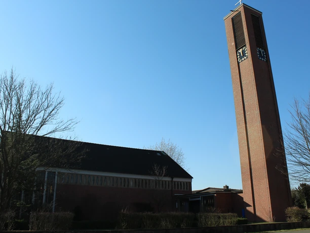 Kreuzkirche Nienburg Backsteinkirche mit hohem Glockenturm, Uhr an der Spitze, blauer Himmel im Hintergrund, Bäume ohne Blätter.