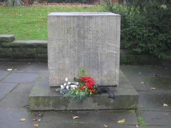 Gedenkstein mit eingraviertem Text, umgeben von Blumen als Zeichen des Gedenkens und der Ehrung.