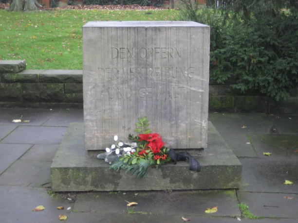 Mahnmal Nienburg Gedenkstein mit eingraviertem Text, umgeben von Blumen als Zeichen des Gedenkens und der Ehrung.
