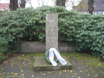 Mahnmal Nienburg Steinernes Kriegerdenkmal mit Kranz in dichter Vegetation, gewidmet den Opfern des Krieges 1939–1945.