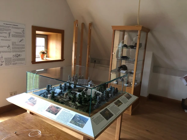 An exhibition space featuring a detailed architectural model in a glass display case, surrounded by information panels.