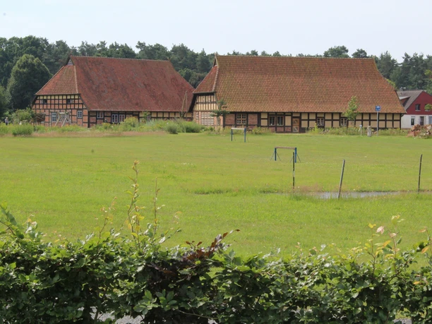 Historic half-timbered buildings at the Ehmken Hoff, surrounded by lush greenery and low hedges in the foreground.