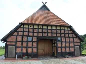 Ehmken Hoff Historisches Fachwerkgebäude mit rotem Ziegeldach und Holztor unter klarem Himmel.