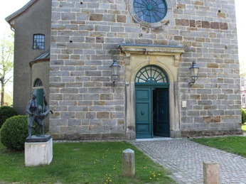 Eingang der historischen Martinskirche mit Skulptur im Vordergrund, eingerahmt von gepflegtem Grün.