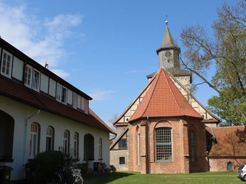 Historische Backsteinkirche mit spitzem Turm und umgebenen Gebäuden unter einem strahlend blauen Himmel.