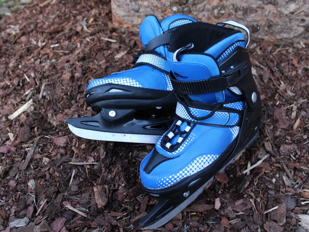 Ein Paar blaue Schlittschuhe mit schwarzen Akzenten liegt auf Rindenmulch vor einem Baumstumpf.