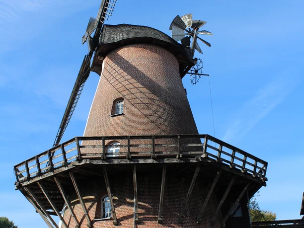 Windmühle Lahde Historische Windmühle mit rotem Ziegelsteinbau und großem Holzdeck vor klarem, blauen Himmel.