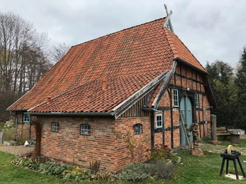 Häuslings Haus Ein altes Fachwerkhaus mit rotem Ziegeldach und grüner Tür steht auf einer gepflegten Rasenfläche.