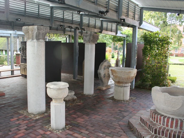 Steingefäße Lapidarium Steingefäße und Säulenreste unter einem überdachten Bereich auf gepflastertem Boden bei Tageslicht.