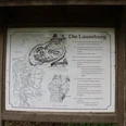 Schild mit Lageplan und Historie der Lasseburg in Landesbergen, umgeben von üppigem Grün.