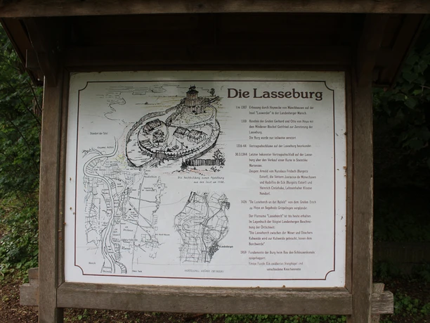 Schild mit Lageplan und Historie der Lasseburg in Landesbergen, umgeben von üppigem Grün.