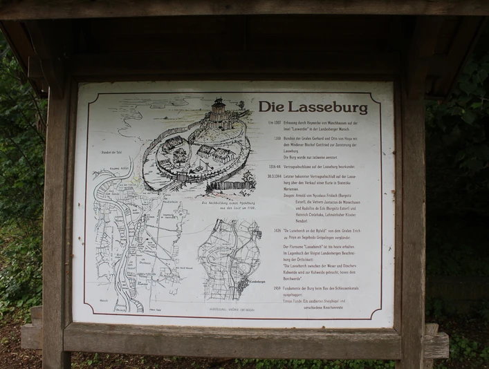 Schild mit Lageplan und Historie der Lasseburg in Landesbergen, umgeben von üppigem Grün.