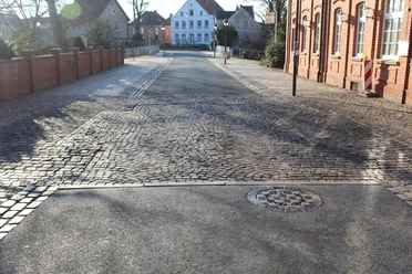 Leintor Straßenansicht mit Kopfsteinpflaster, flankiert von roten Backsteinhäusern und einem weißen Gebäude.